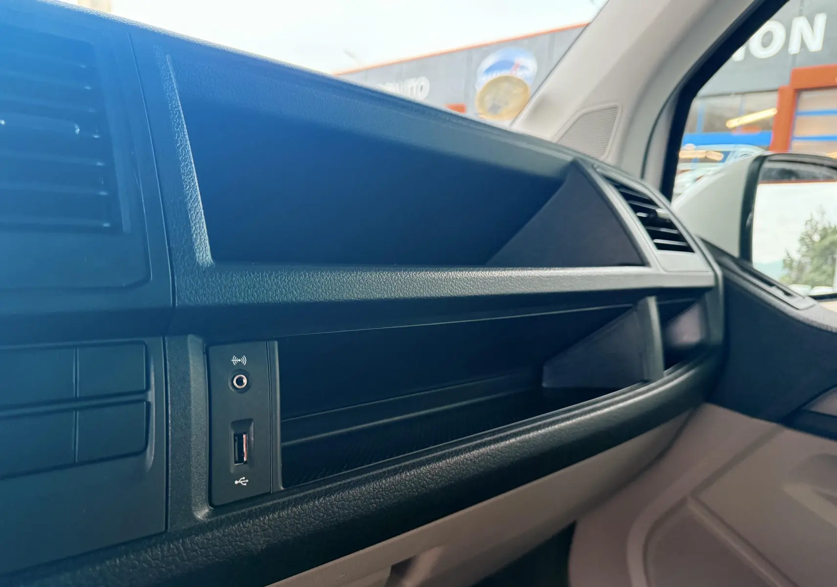 Vue intérieure côté passager du tableau de bord noir du Volkswagen Transporter blanc, avec prise USB visible.