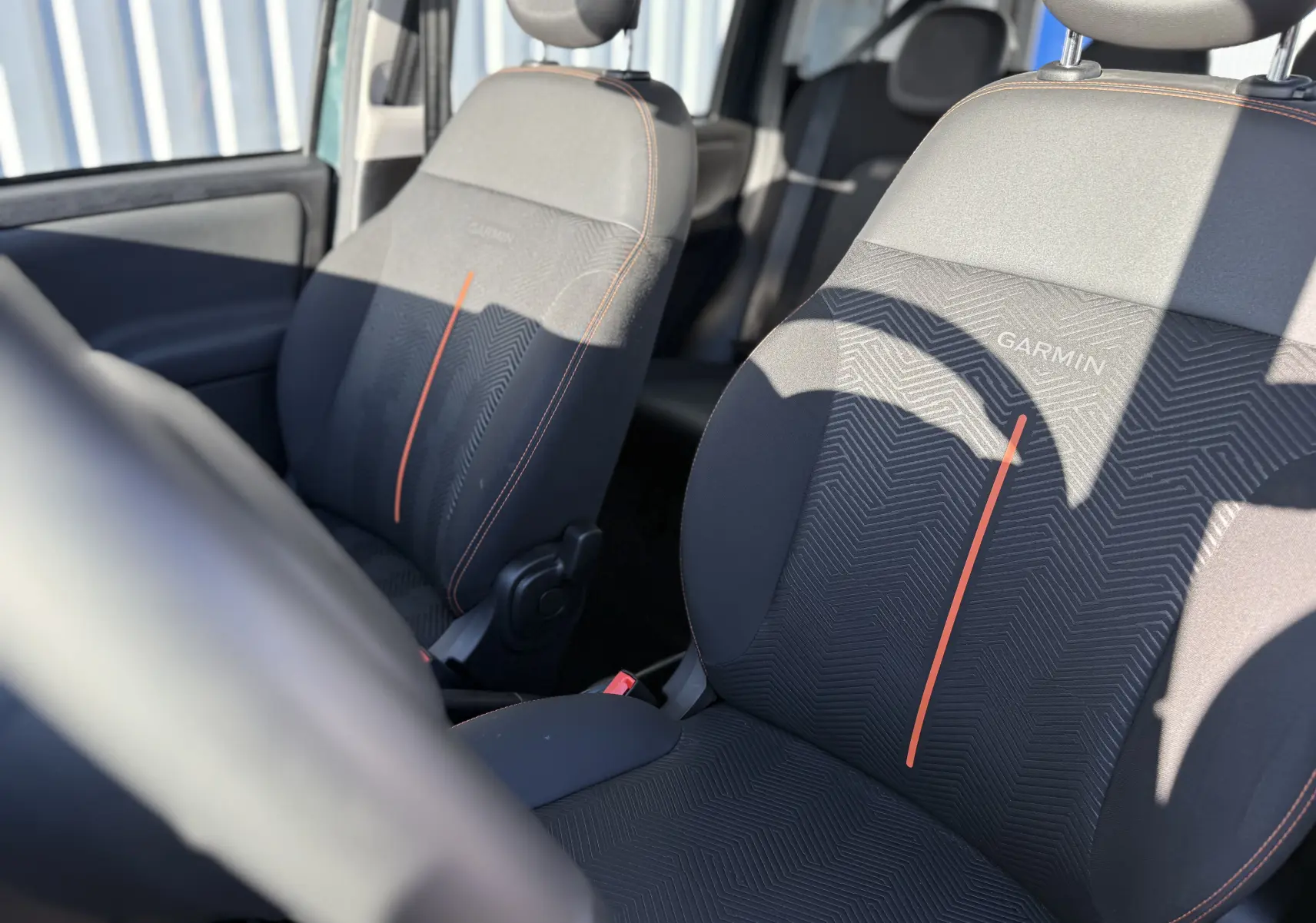 Gros plan sur les sièges avant noirs avec surpiqûres orange et logo Garmin, intérieur de la Fiat Panda City Cross 2023.