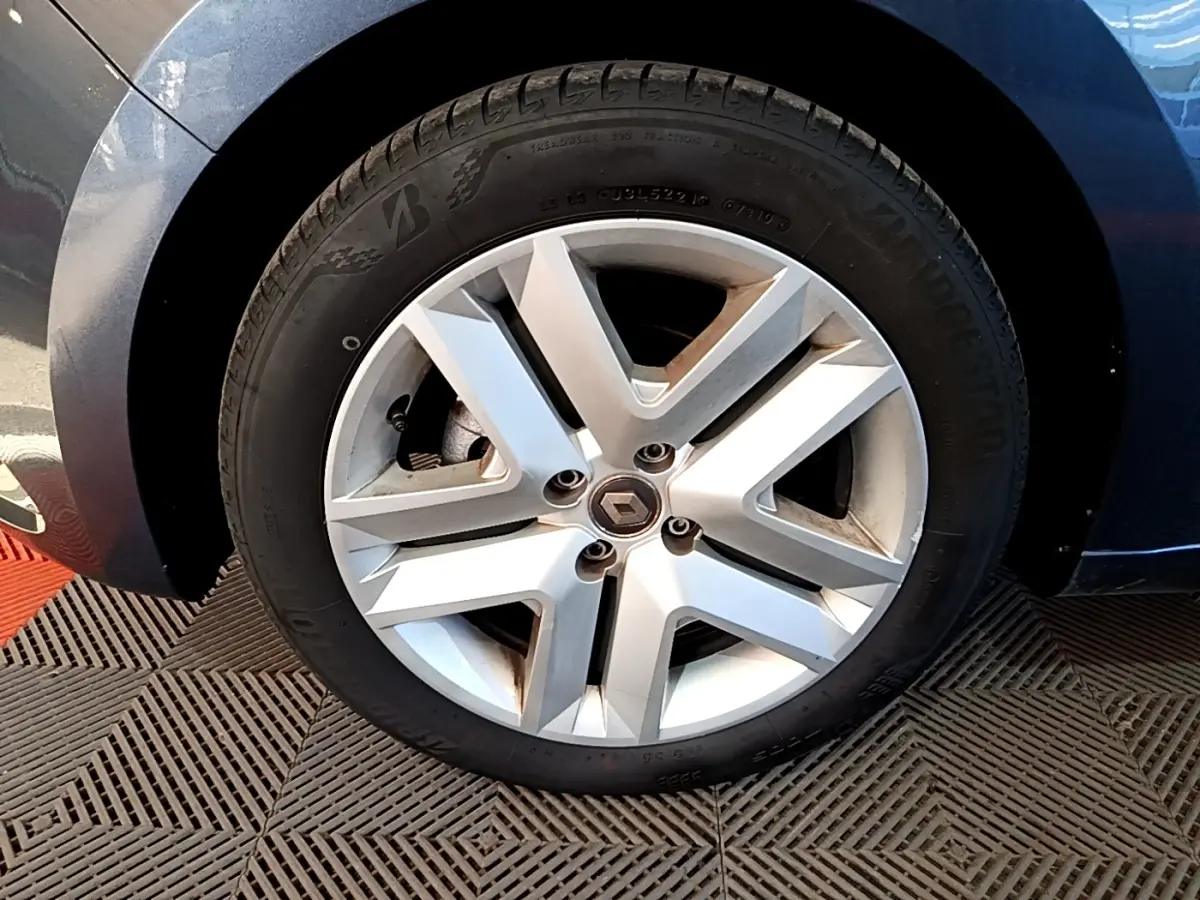 Gros plan sur la roue avant gauche d'une Renault Clio gris foncé, jante alliage au design moderne à cinq branches.