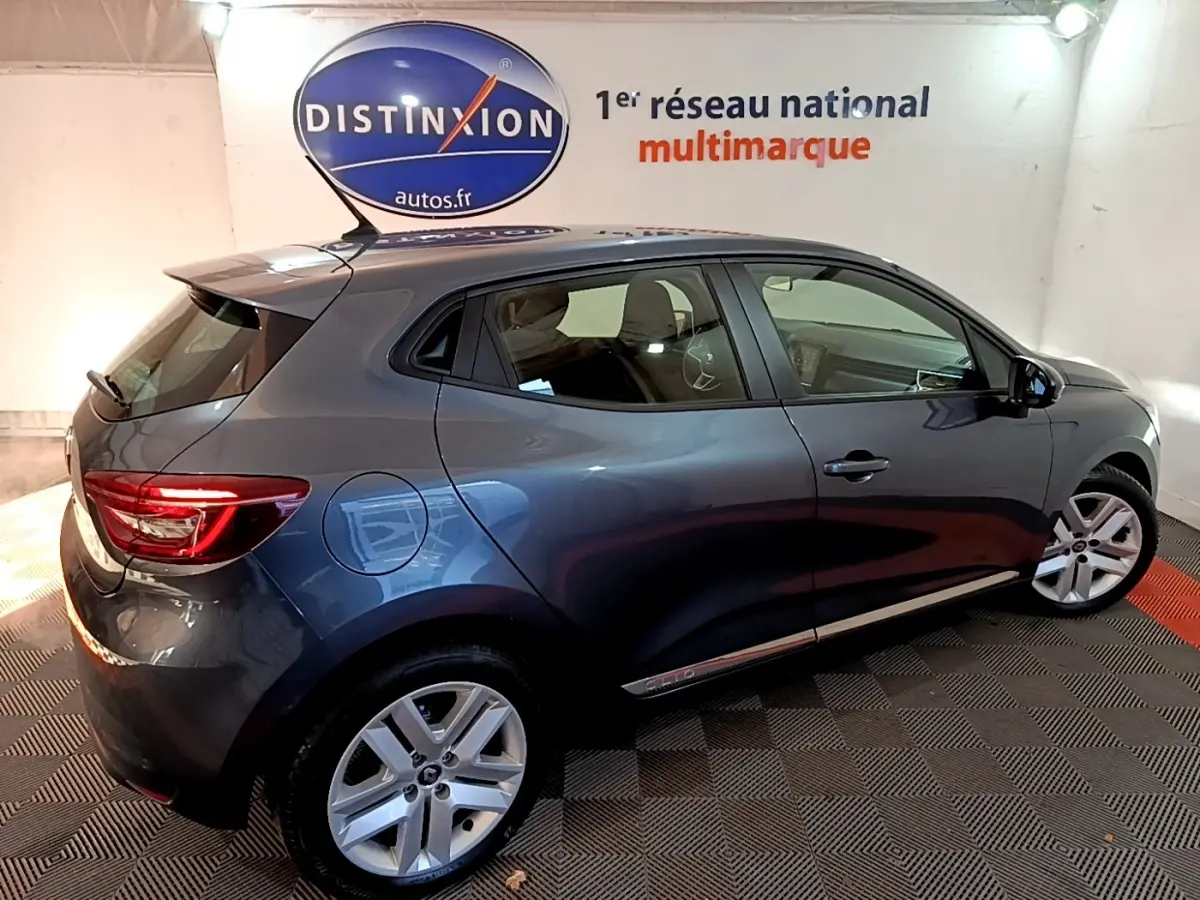 Renault Clio Business TCe 90 gris foncé vue de profil droit en intérieur avec jantes alliage et feux arrière allumés.