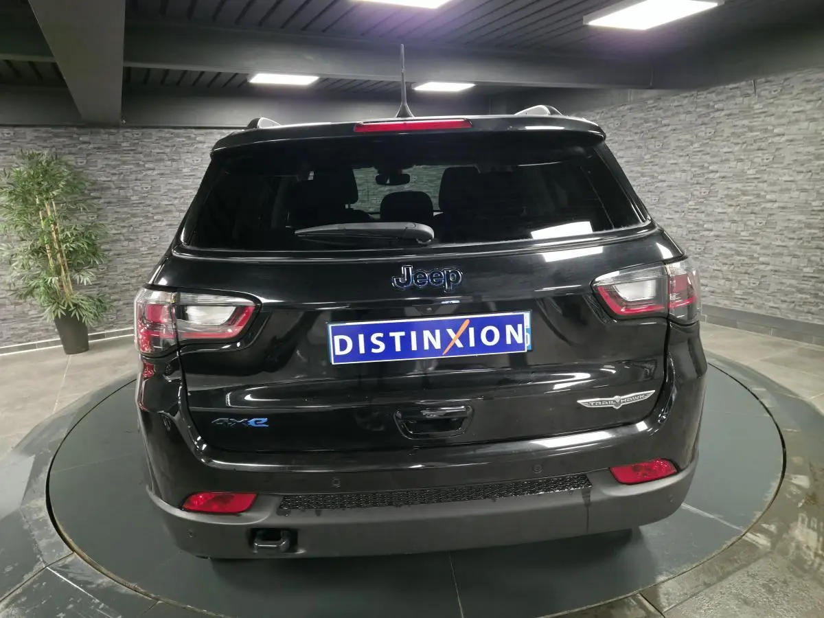 Vue arrière d'un Jeep Compass Trailhawk noir brillant avec badges Trailhawk et 4xe en intérieur showroom.