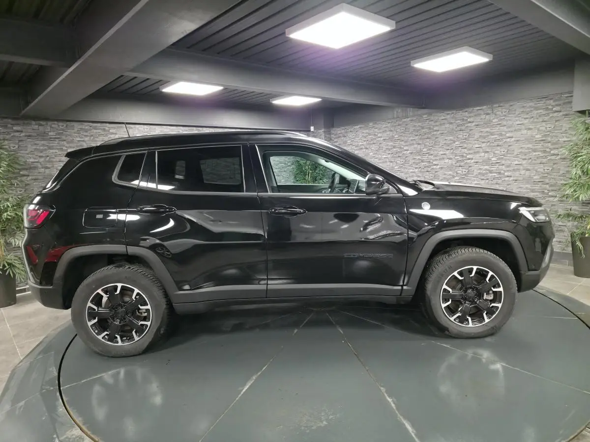 Vue de profil côté gauche d'un Jeep Compass Trailhawk noir avec jantes alliage et stickers distinctifs en intérieur showroom.