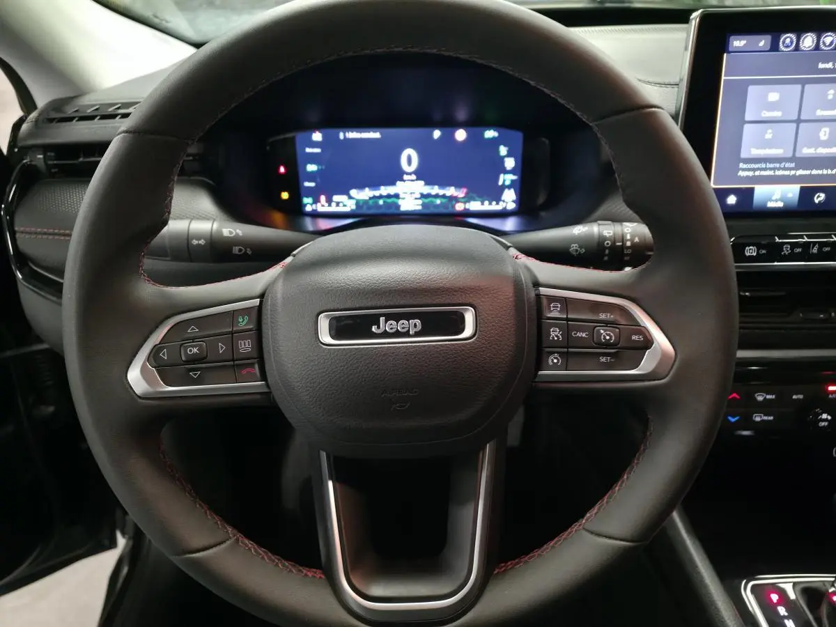 Vue rapprochée du volant cuir noir avec surpiqûres rouges et tableau de bord numérique du Jeep Compass Trailhawk 2024.