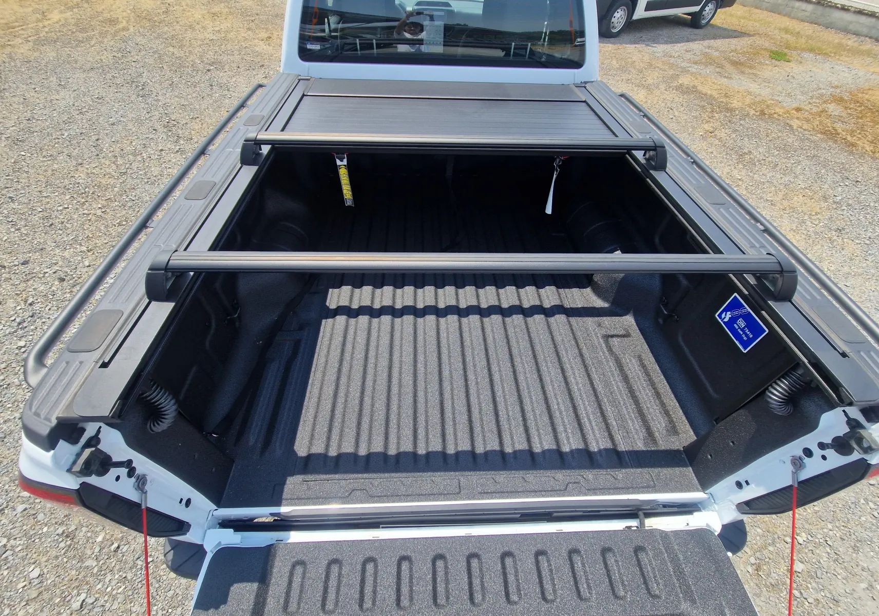 Vue plongeante sur le plateau ouvert du Ford Ranger Super Cabine blanc, avec rideau rigide coulissant et barres de maintien.
