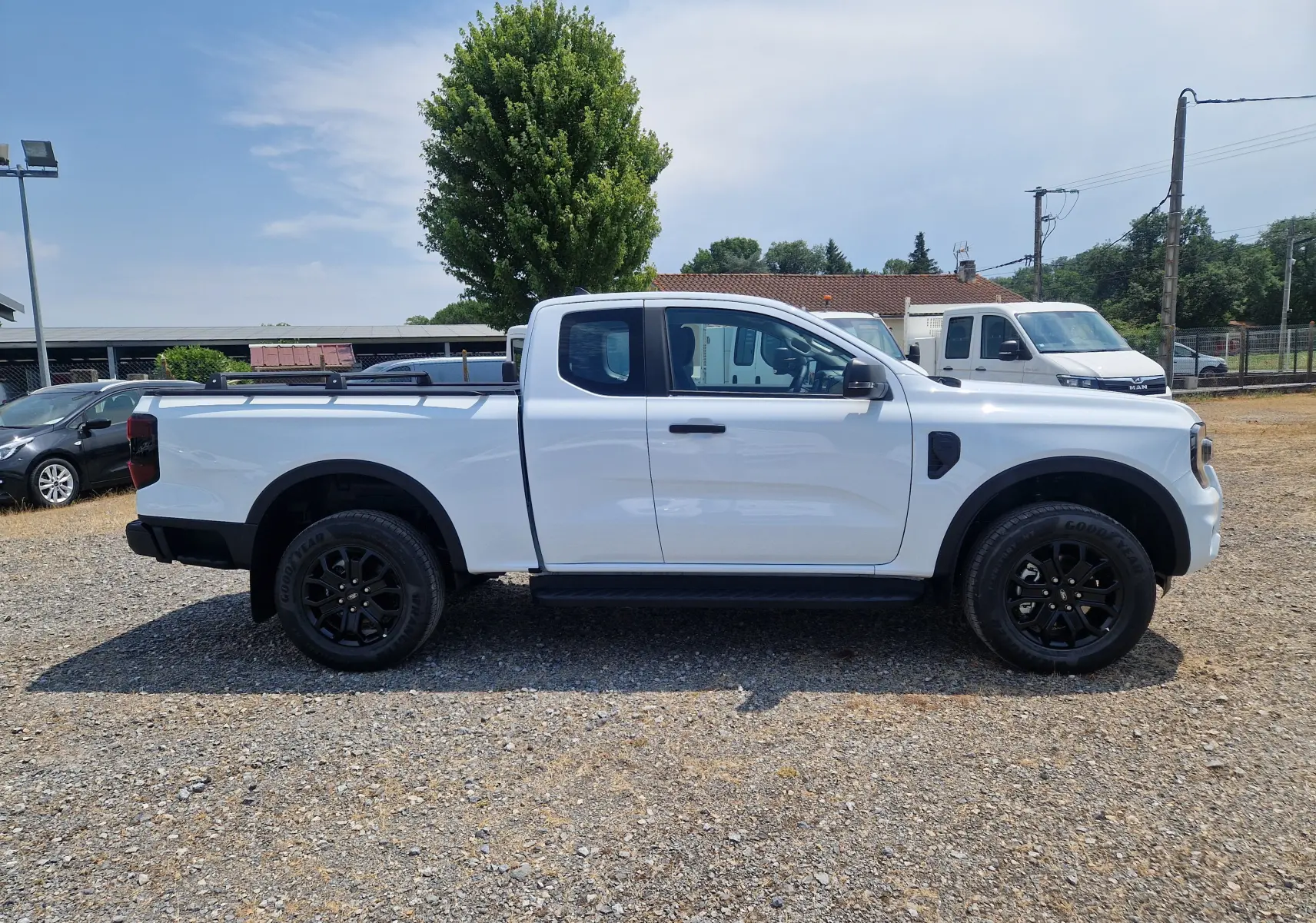 Ford Ranger Super Cabine blanc vu de profil côté gauche, avec plateau équipé de barres et rideau rigide coulissant.