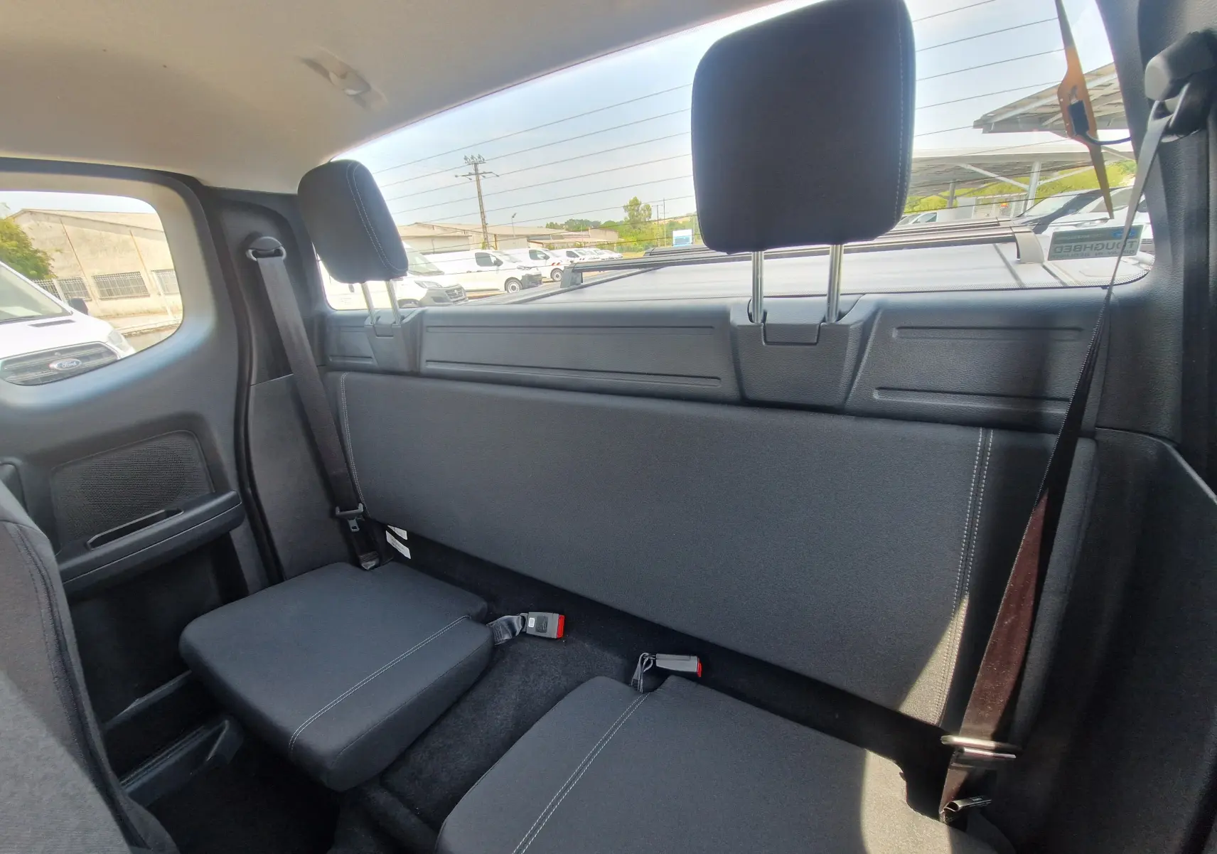 Vue intérieure arrière du Ford Ranger Super Cabine blanc, montrant les sièges arrière rabattus et la banquette compacte.