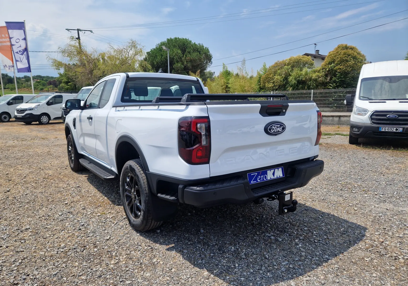 Vue 3/4 arrière droite du Ford Ranger Super Cabine blanc avec rideau de plateau rigide et barres sur le plateau.