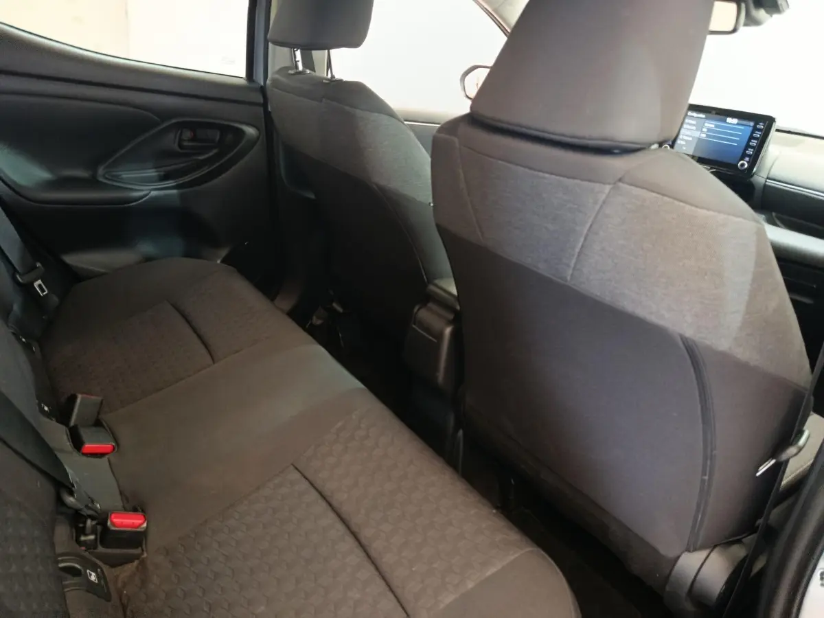 Vue intérieure arrière de la Toyota Yaris Hybride 116h Design 2023, sièges tissu noir et tableau de bord avec écran tactile.