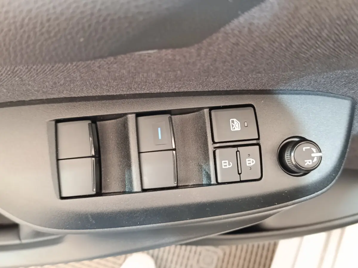 Gros plan sur les commandes de lève-vitres et réglage des rétroviseurs côté conducteur d'une Toyota Yaris hybride gris clair 2023.