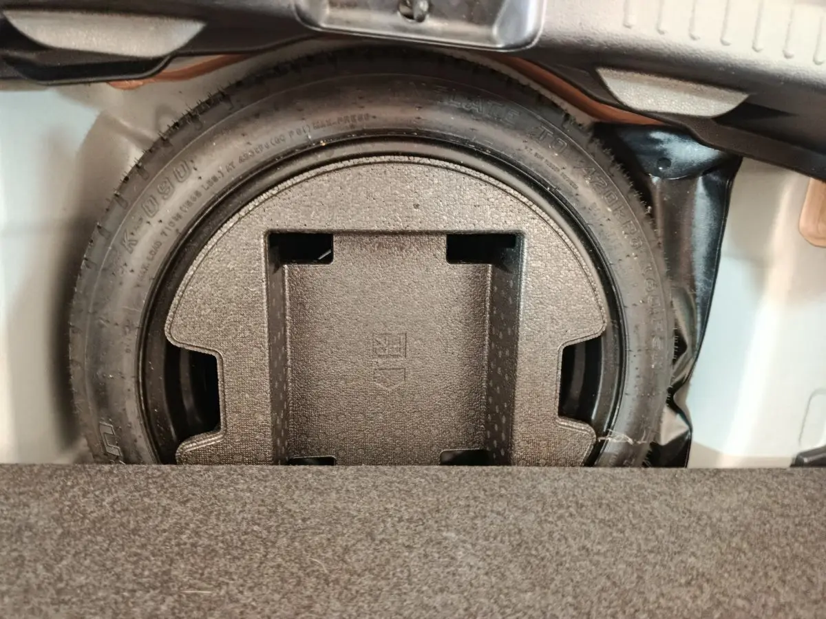 Gros plan sur la roue de secours dans le coffre d'une Toyota Yaris hybride gris clair, vue de dessus.