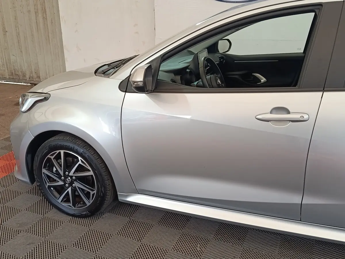 Vue latérale côté gauche d'une Toyota Yaris hybride gris clair avec jante alliage noir et intérieur visible.