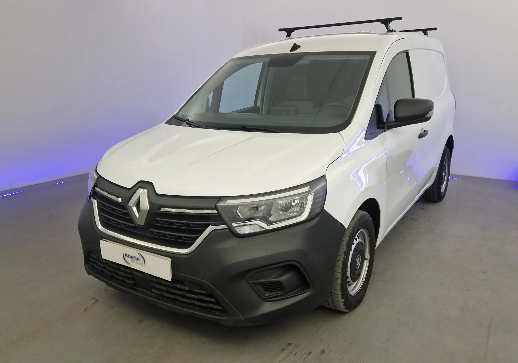 Renault Kangoo Van blanc vue 3/4 avant droit, avec calandre noire et barres de toit visibles.
