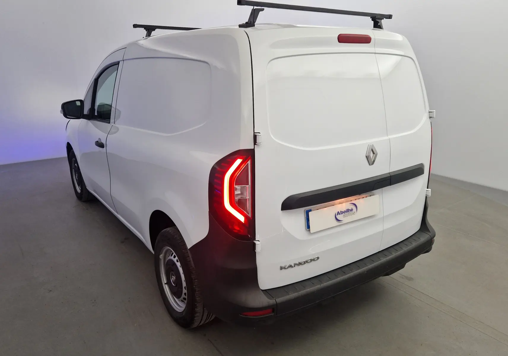 Vue 3/4 arrière droite d’un Renault Kangoo blanc 2023 avec feux arrière allumés et galerie de toit noire.