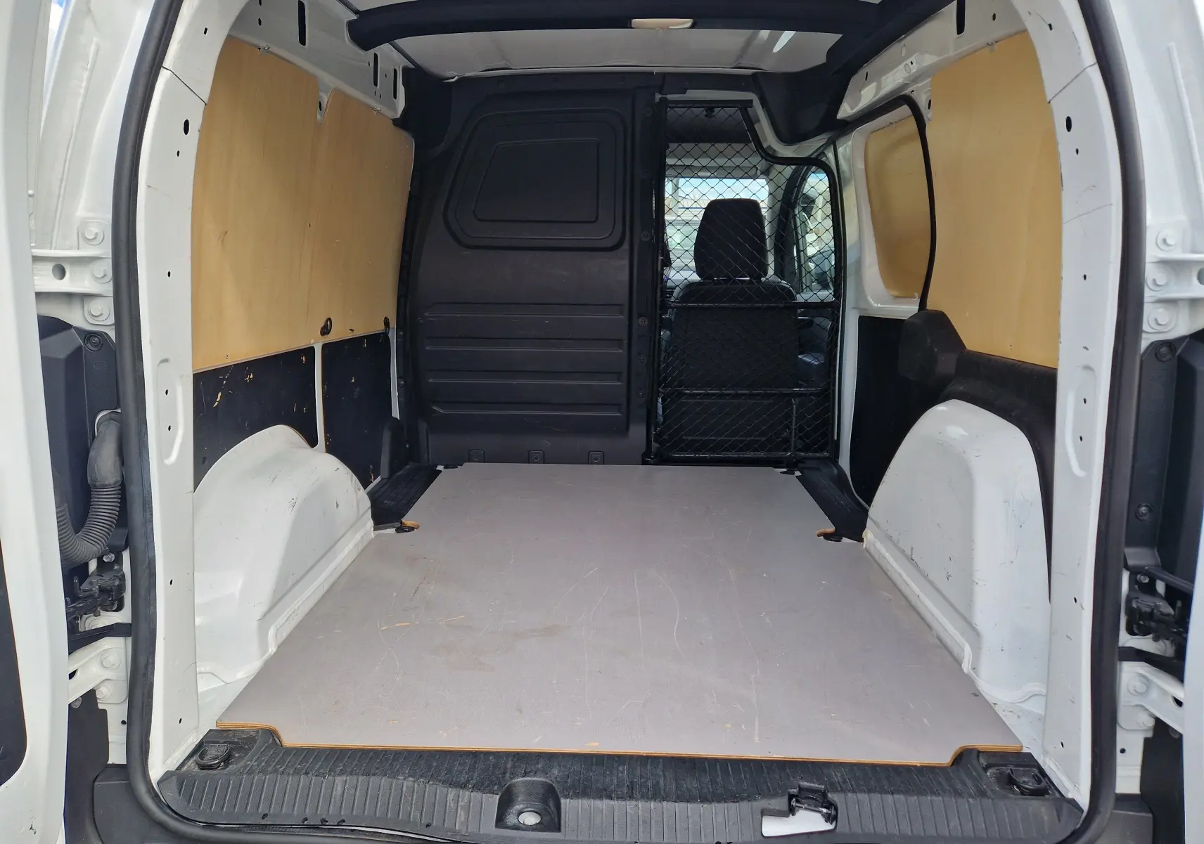 Vue intérieure arrière du Renault Kangoo blanc 2023, montrant l’espace de chargement avec grille de séparation et panneaux bois.