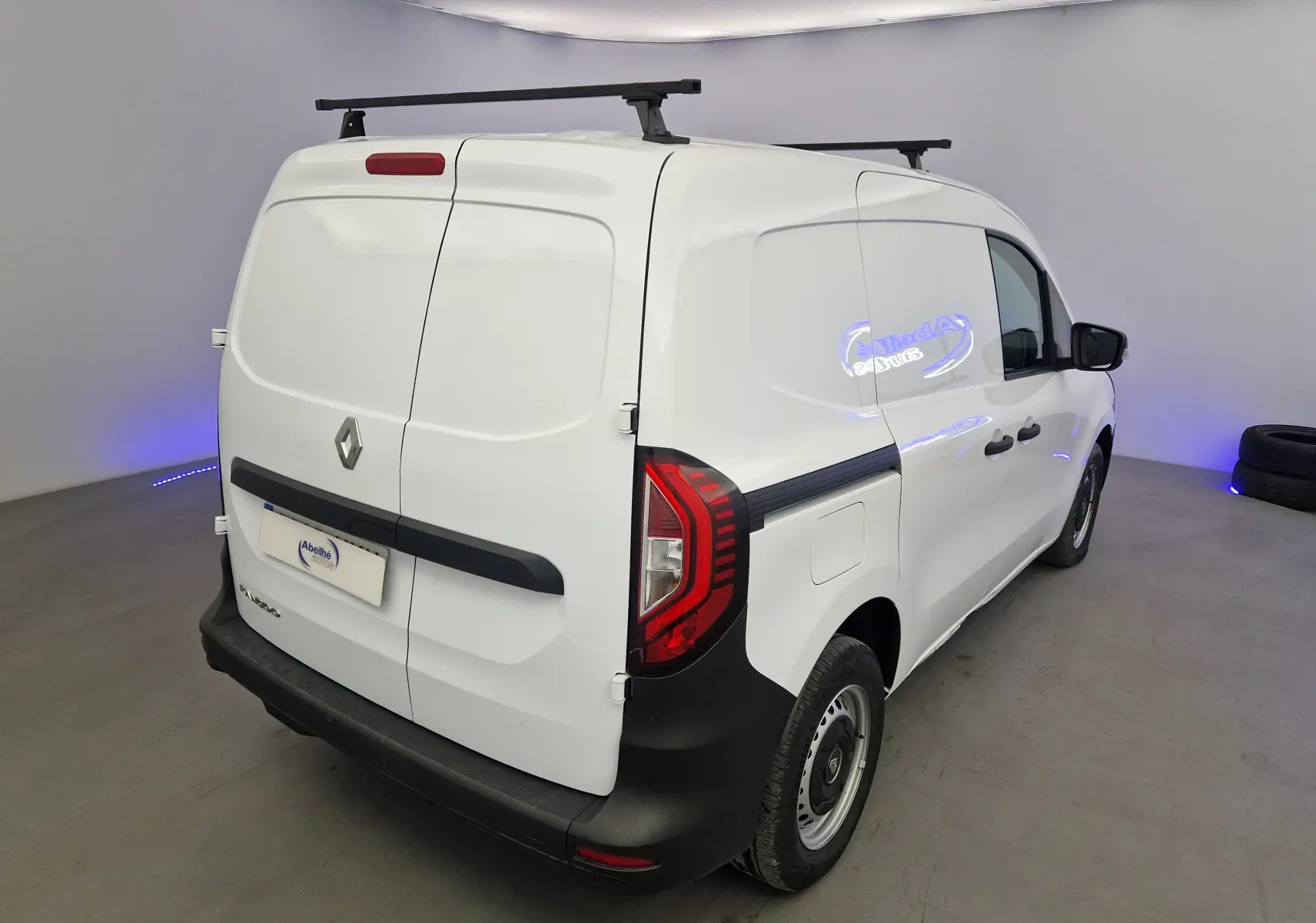 Renault Kangoo Van blanc vu en 3/4 arrière droit, avec barres de toit et feux arrière rouges distinctifs.