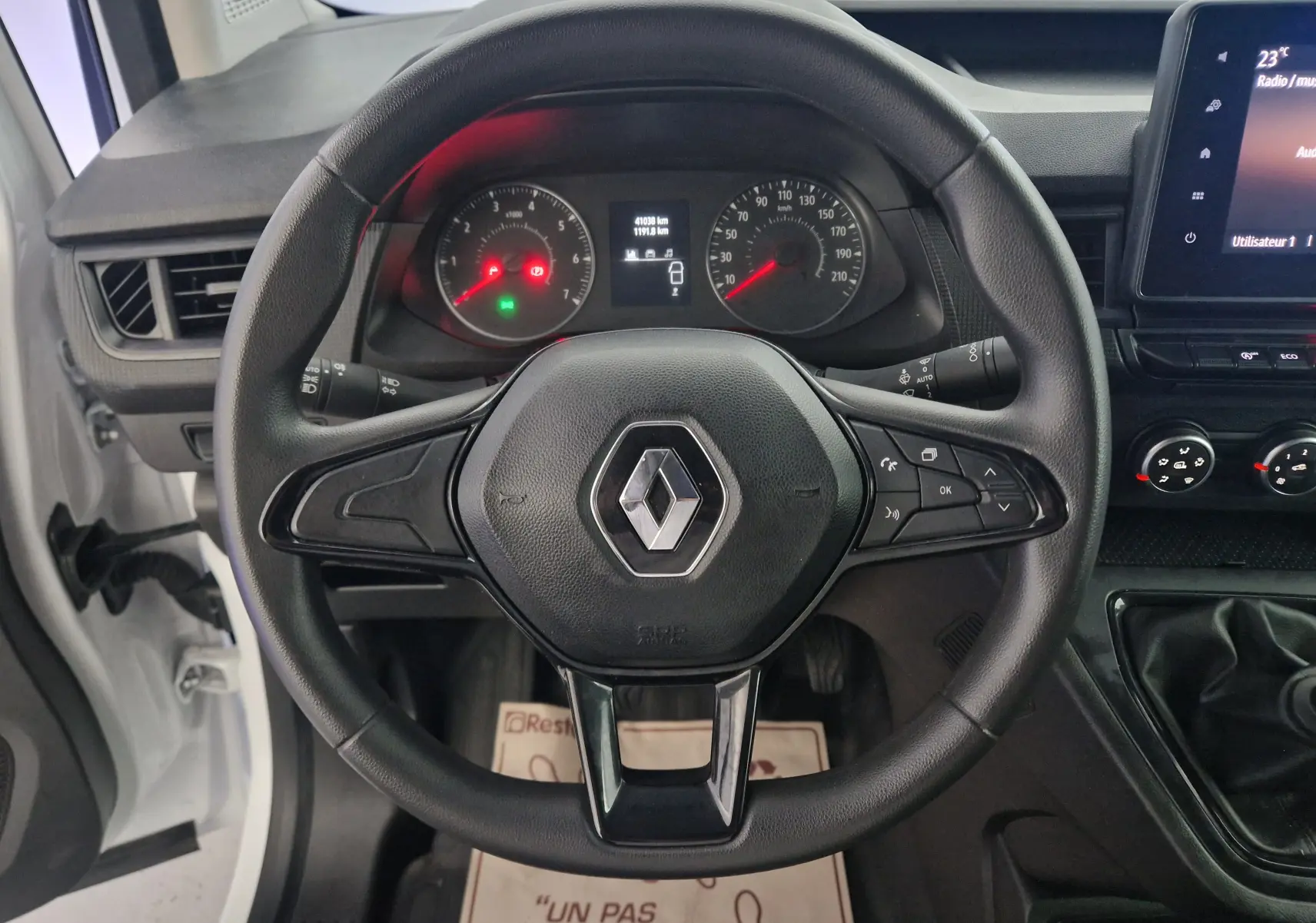 Vue rapprochée du volant noir du Renault Kangoo blanc 2023, avec tableau de bord et commandes visibles.