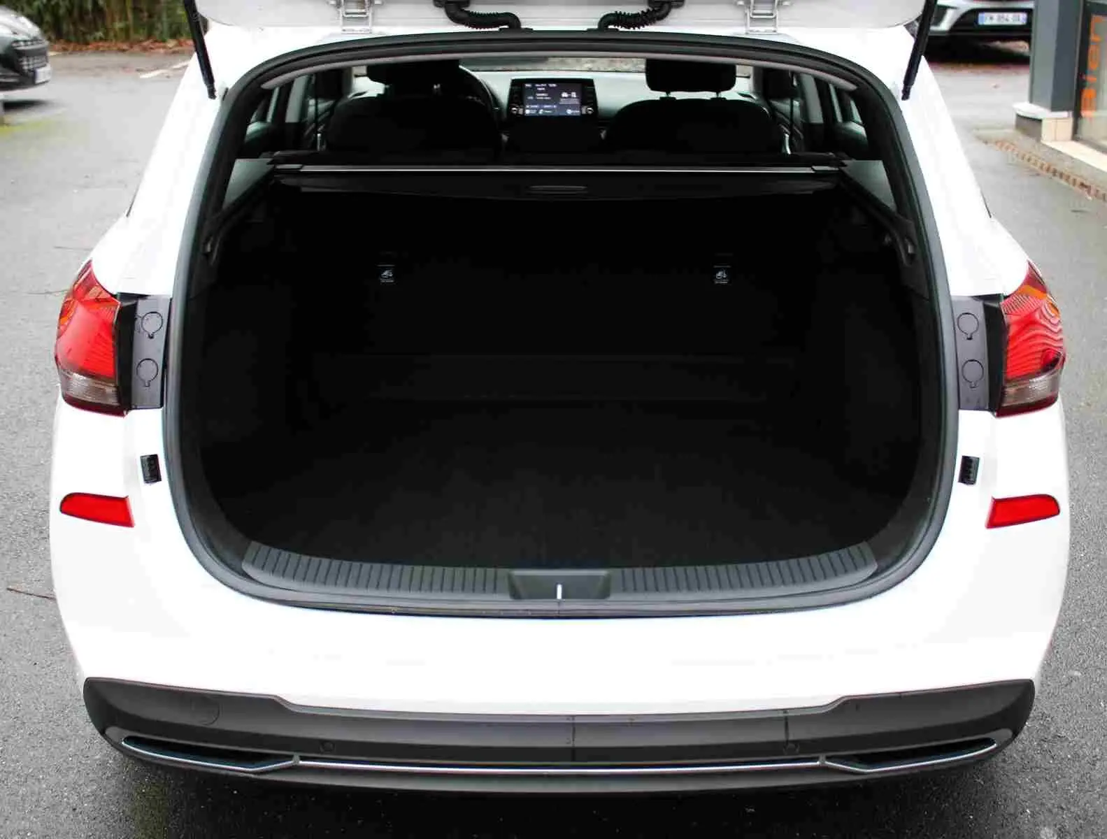 Vue arrière ouverte du coffre d'une Hyundai i30 SW blanche polaire, montrant l'espace de chargement et l'intérieur sombre.