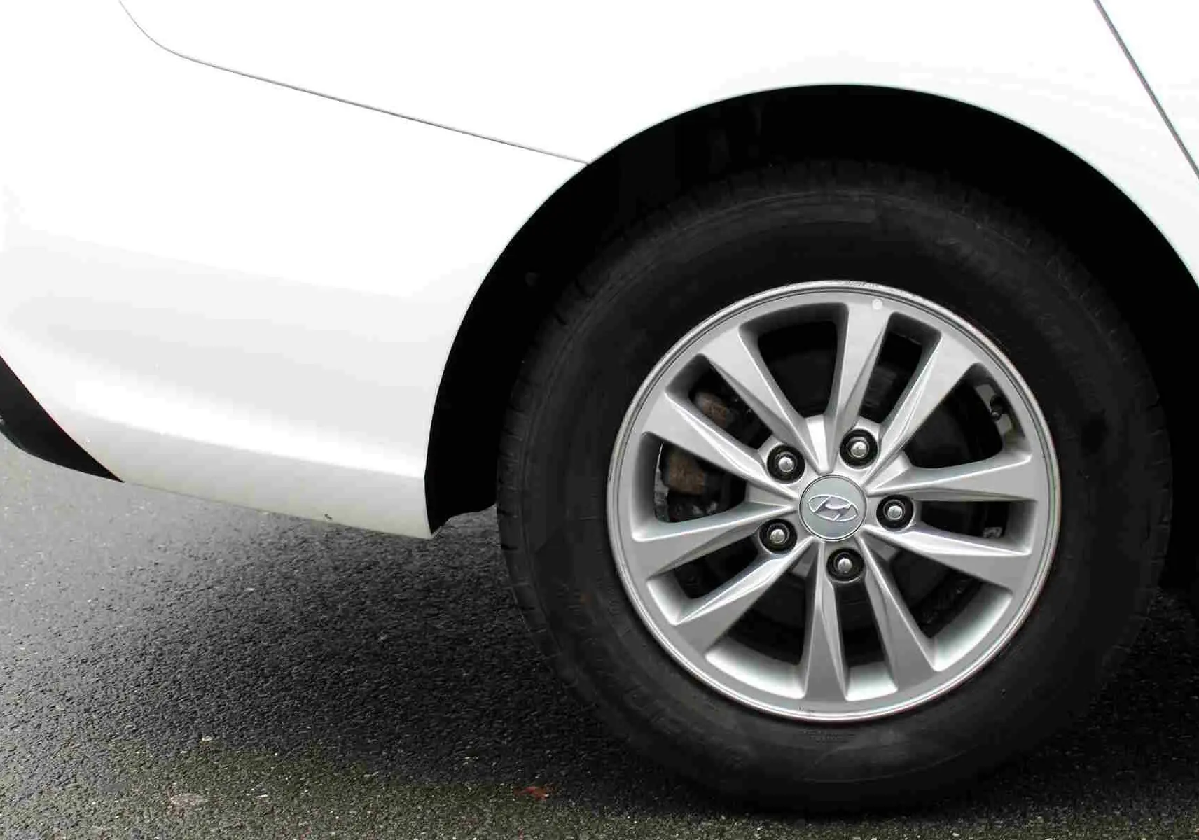 Gros plan sur la roue arrière droite d'une Hyundai i30 SW blanche polaire, mettant en valeur la jante alliage 15 pouces.