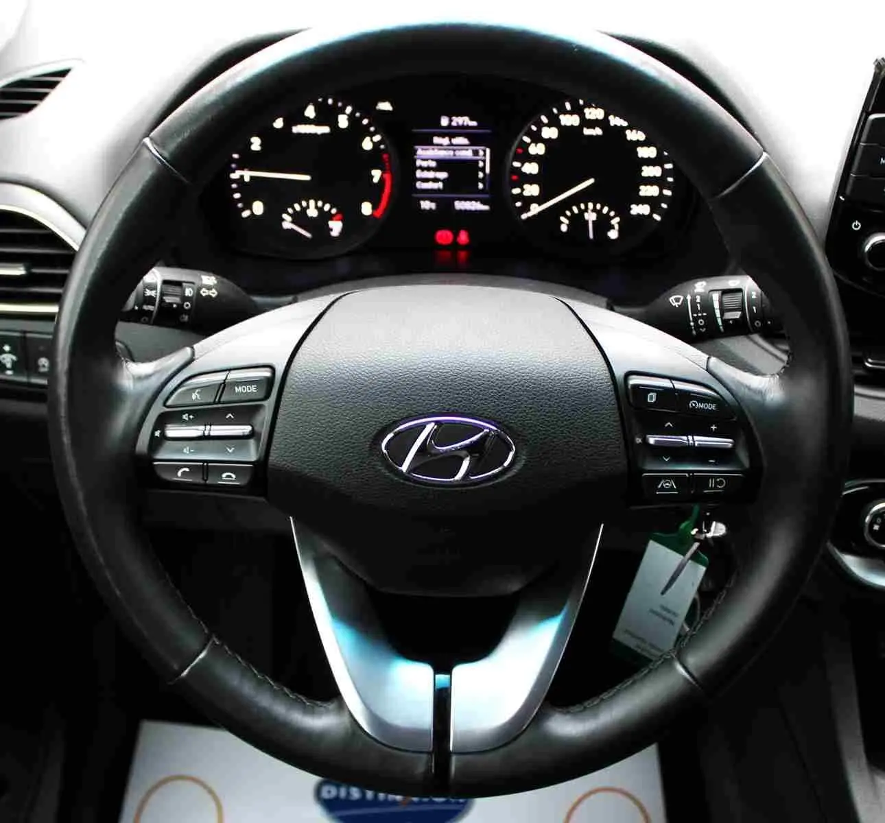 Vue rapprochée du volant noir de la Hyundai i30 SW 2022 avec commandes intégrées et tableau de bord éclairé en arrière-plan.