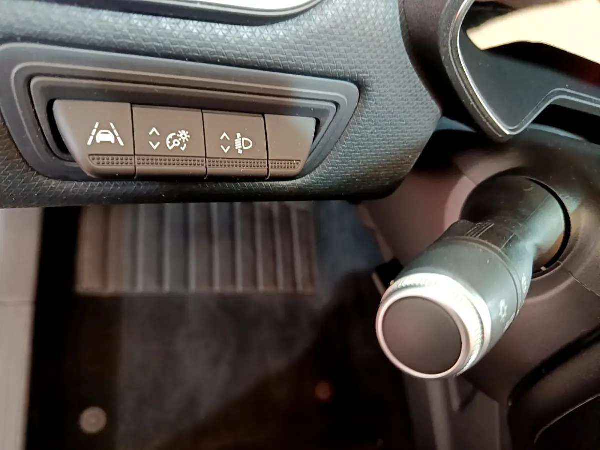 Gros plan sur les commandes d'assistance et réglage des phares à gauche du volant dans l'habitacle noir de la Renault Clio Business 2020.