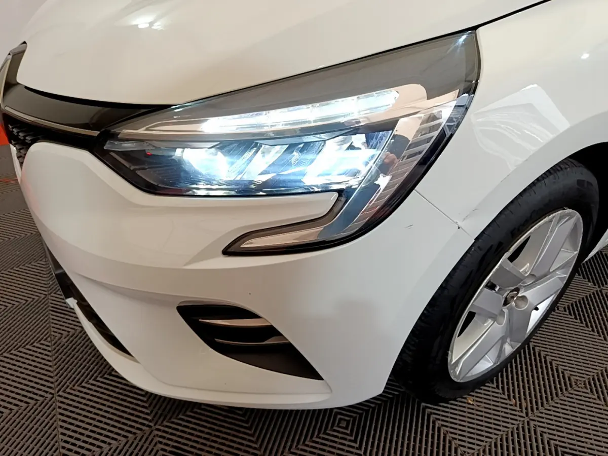 Gros plan sur l'avant droit d'une Renault Clio Business TCe 100 blanche, mettant en valeur le phare LED et la jante alliage.
