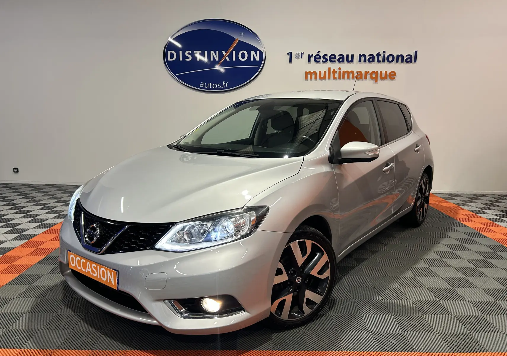 Nissan Pulsar gris vue 3/4 avant droit avec phares allumés et jantes alliage noires et argentées.