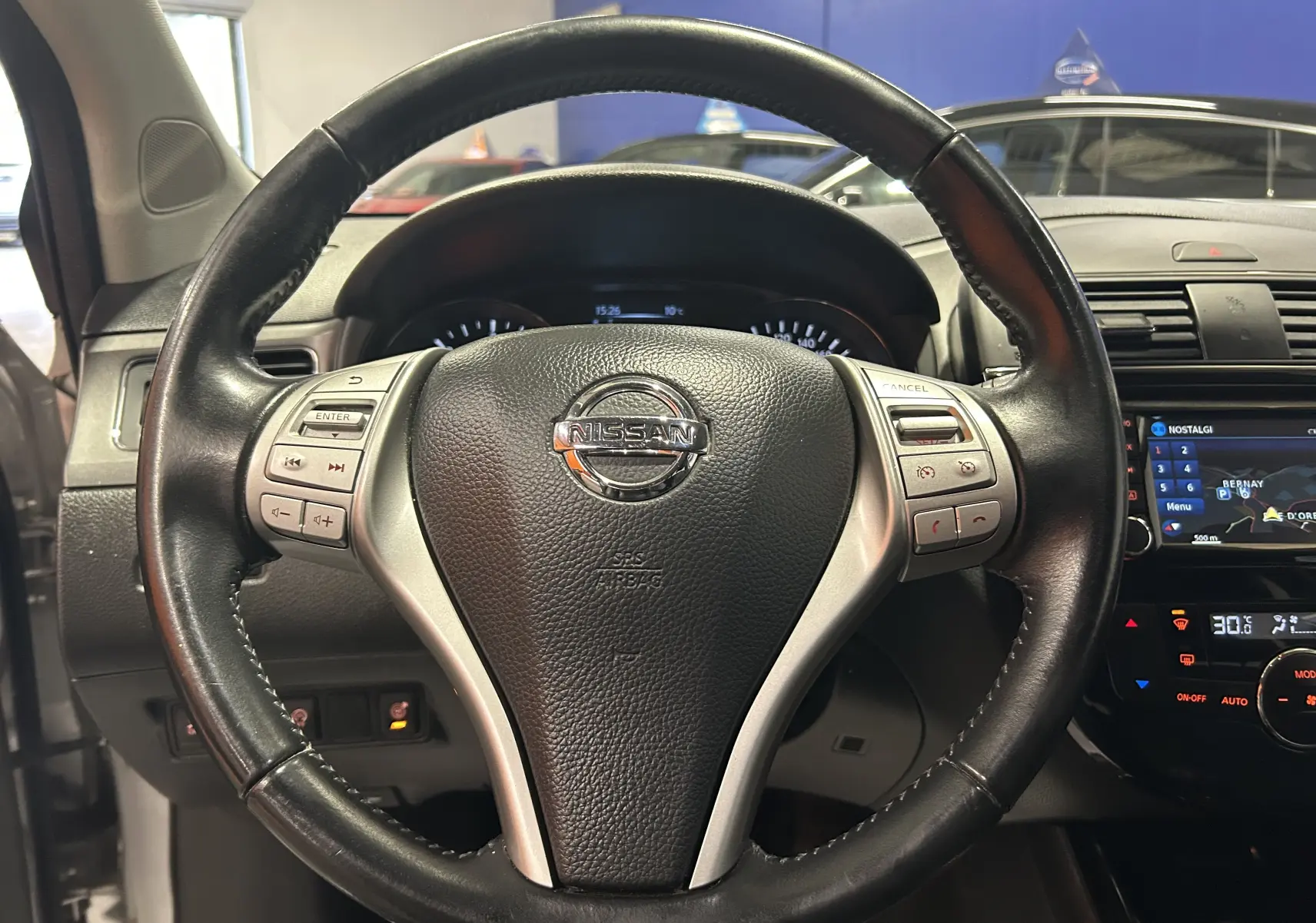 Vue centrée sur le volant cuir noir de la Nissan Pulsar 2018 avec tableau de bord et écran GPS visible à droite.