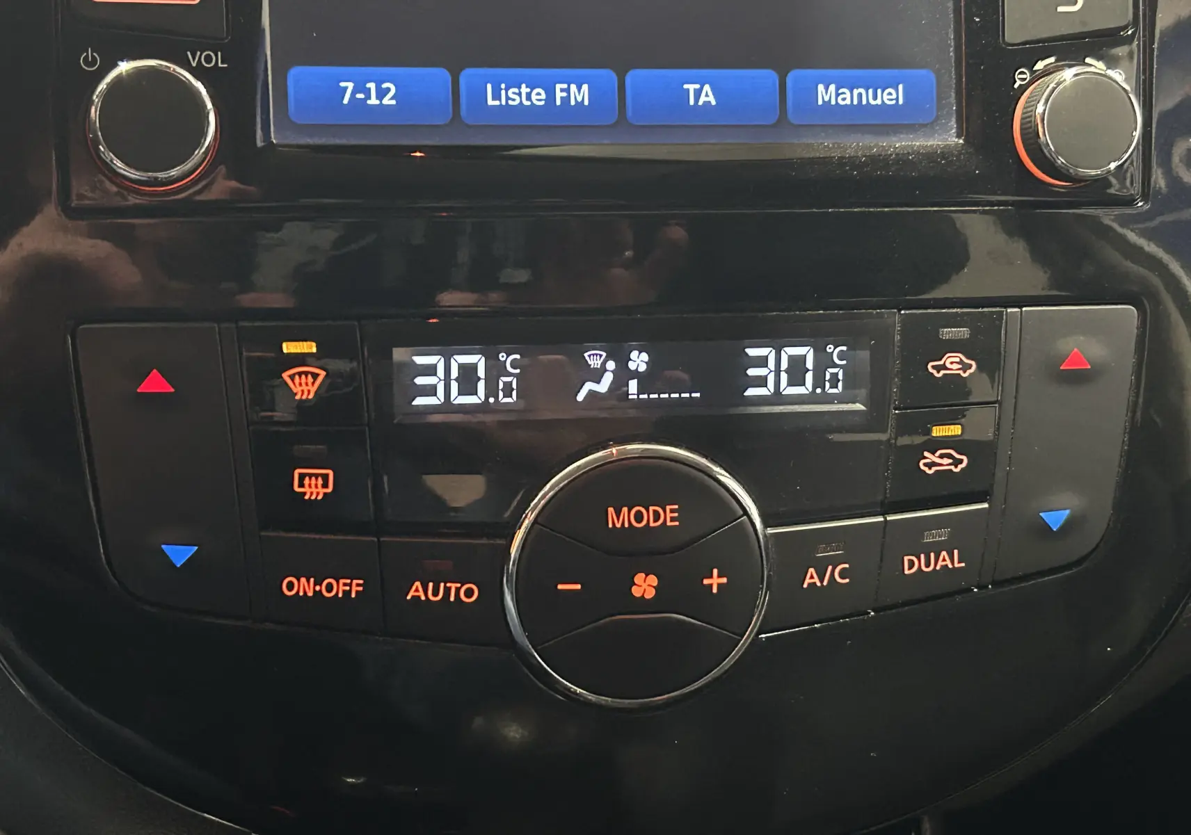 Gros plan sur la console centrale noire de la Nissan Pulsar 2018, affichant la climatisation digitale à 30°C en mode dual.