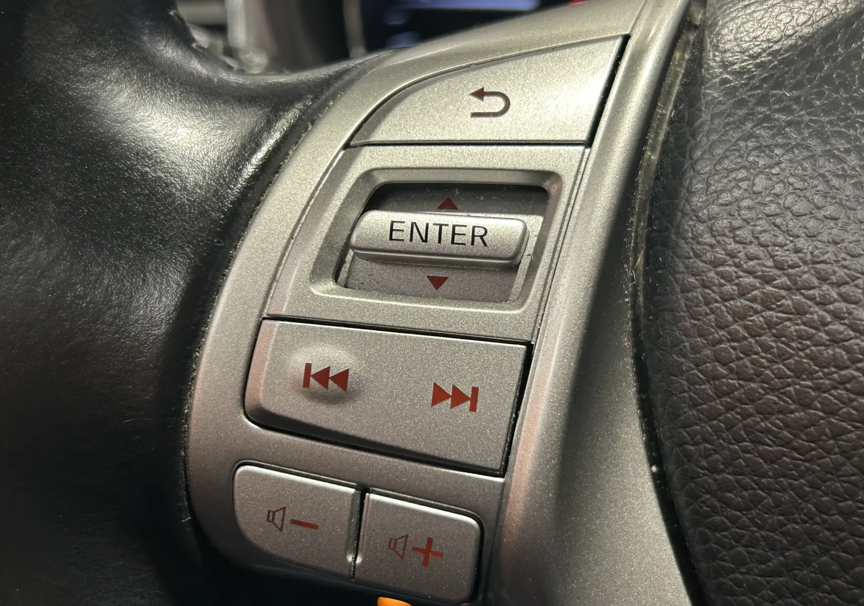 Gros plan sur les commandes argentées du volant en cuir noir du Nissan Pulsar gris, version 2018.