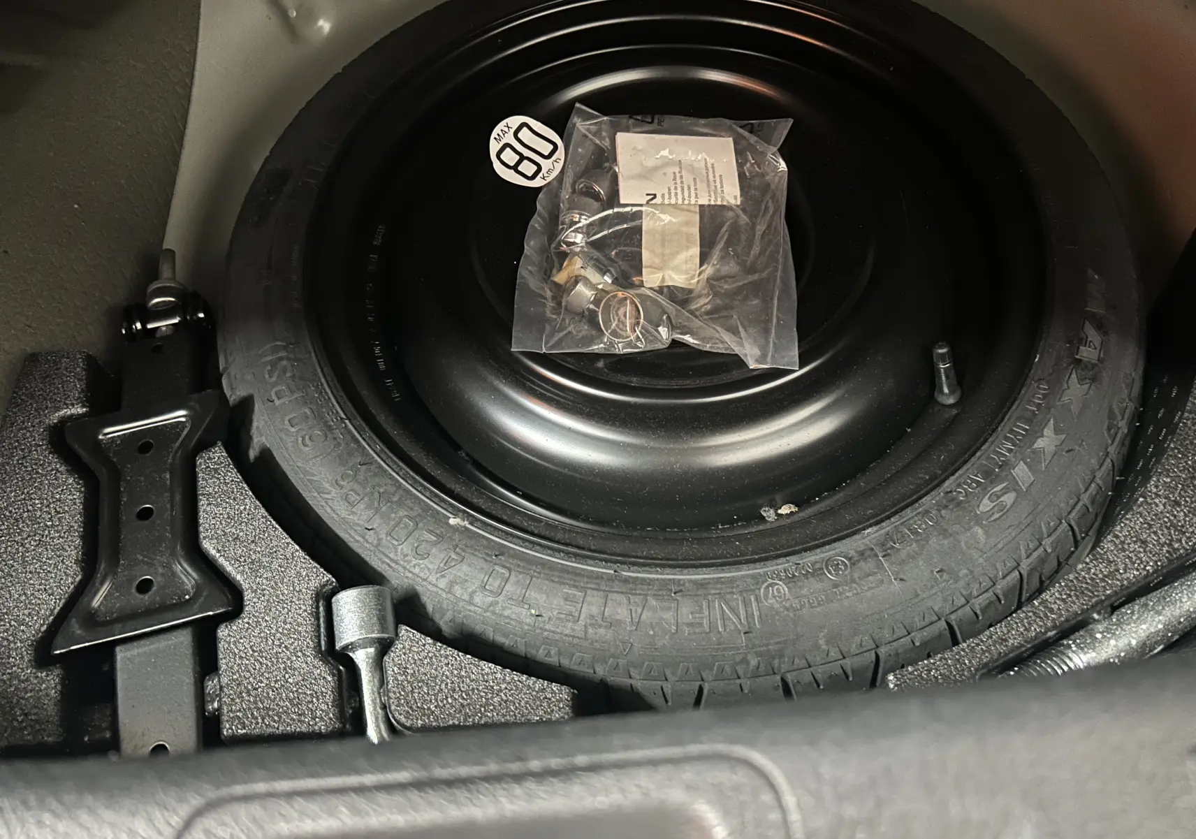 Vue rapprochée de la roue de secours noire et de ses outils dans le coffre du Nissan Pulsar gris 2018.