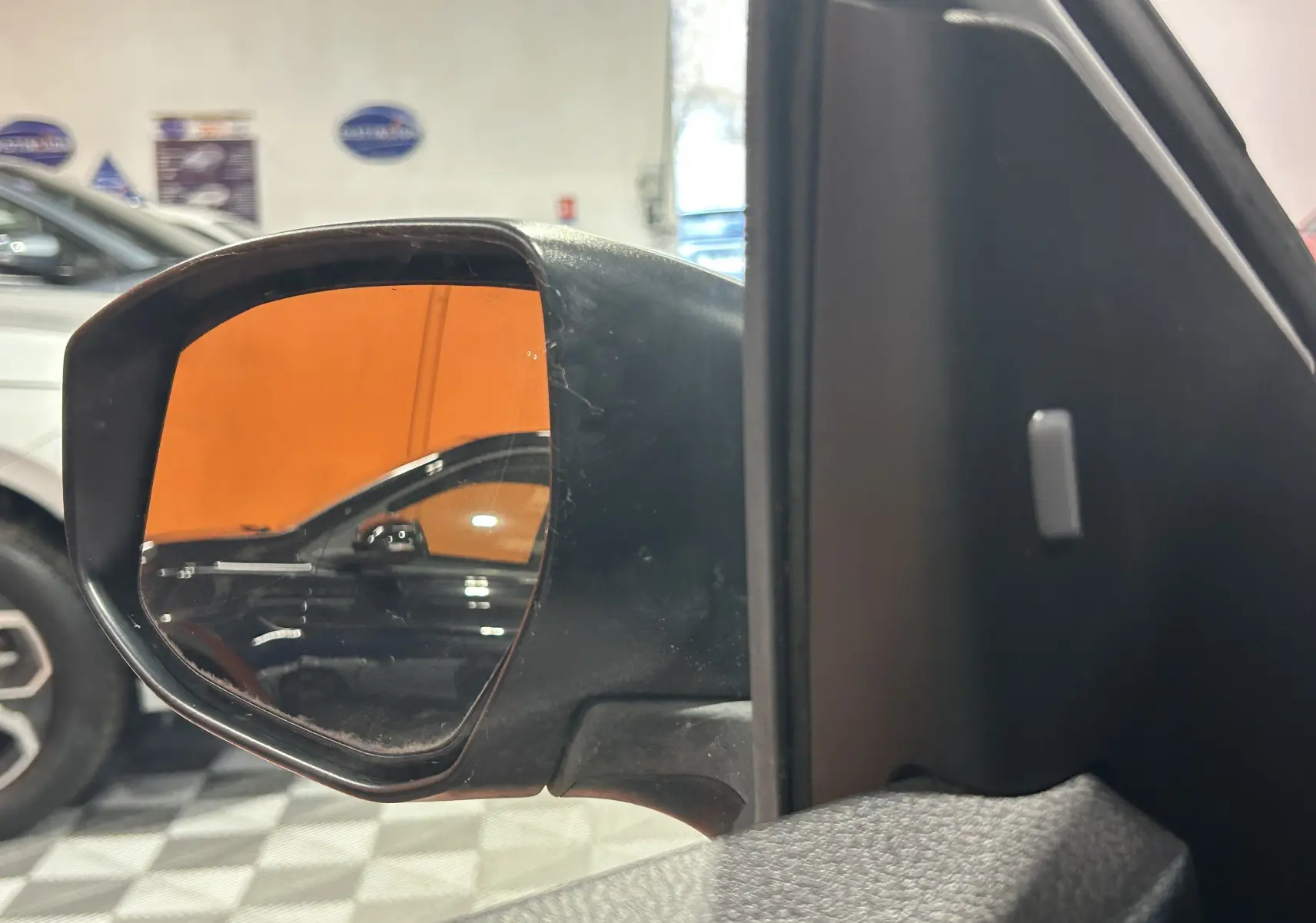 Rétroviseur extérieur côté gauche d’une Nissan Pulsar gris, avec reflet d’un autre véhicule noir en arrière-plan.