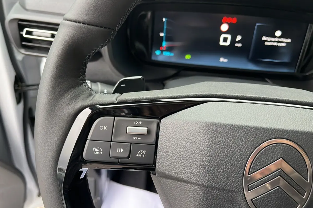 Gros plan sur le volant cuir multifonctions du Citroën Berlingo blanc Kaolin, avec commandes et écran numérique en arrière-plan.