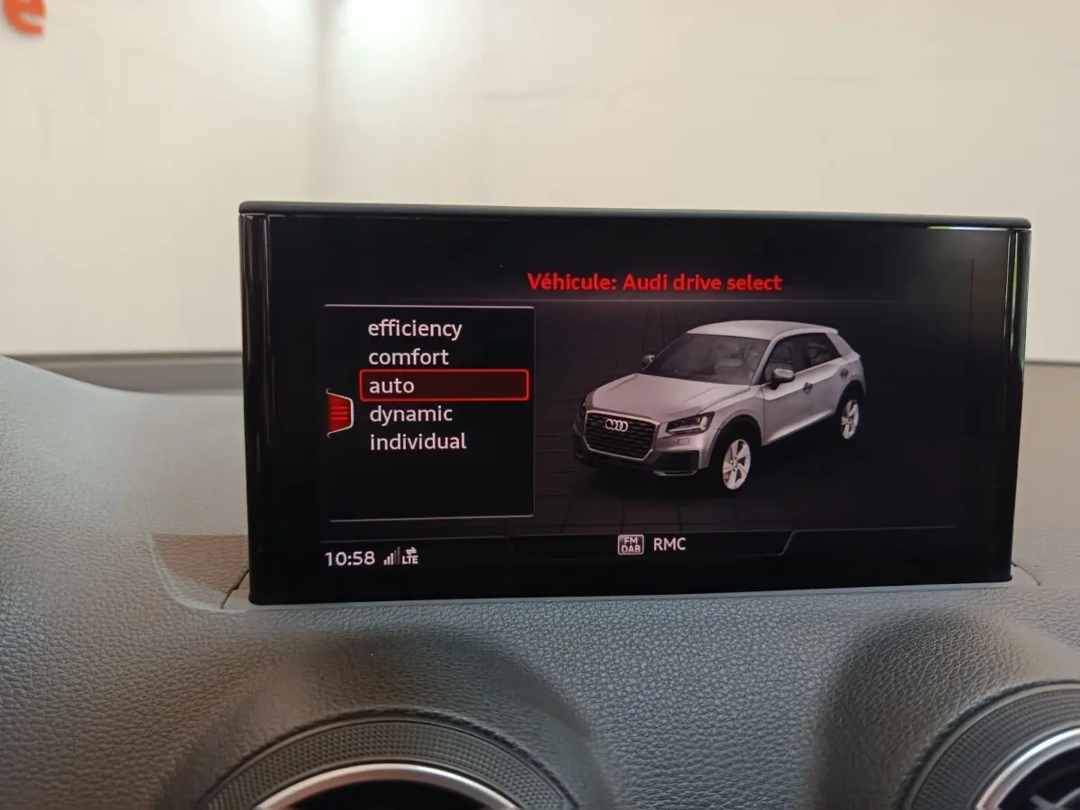 Écran tactile intérieur montrant une Audi Q2 gris clair en vue 3/4 avant droite avec modes de conduite sélectionnables.