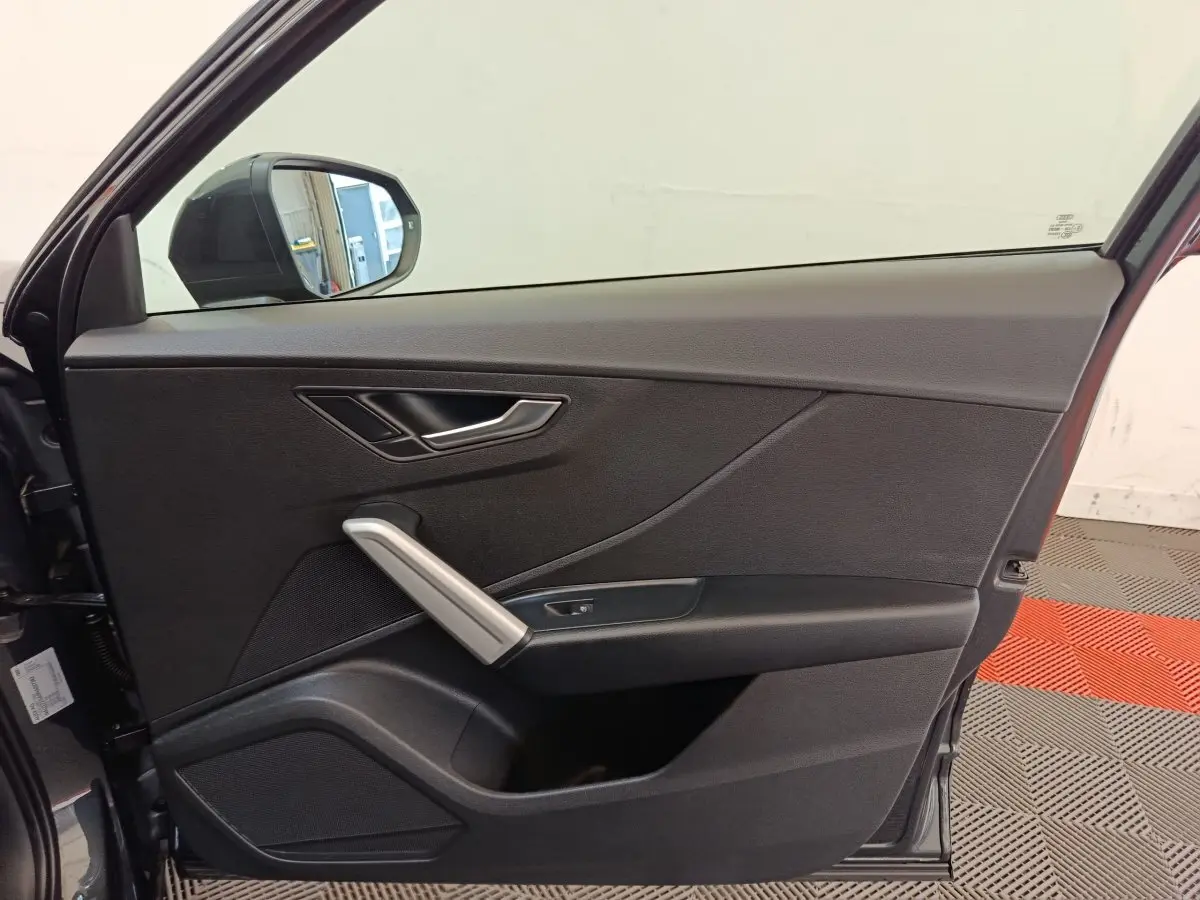 Vue côté intérieur de la porte avant gauche de l'Audi Q2 gris foncé, avec poignée argentée et miroir extérieur visible.