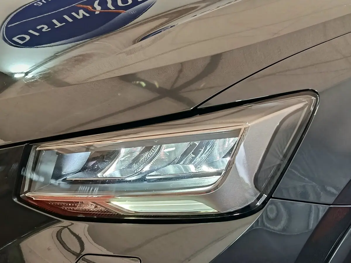 Gros plan sur le phare avant droit d’un Audi Q2 gris foncé, mettant en valeur son design LED moderne.