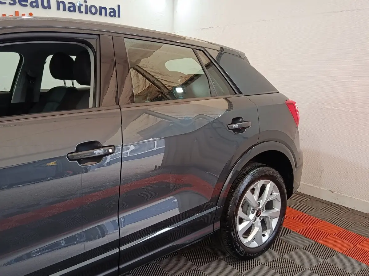 Vue côté droit arrière d'un Audi Q2 gris foncé avec jantes alliage et poignées de porte noires.