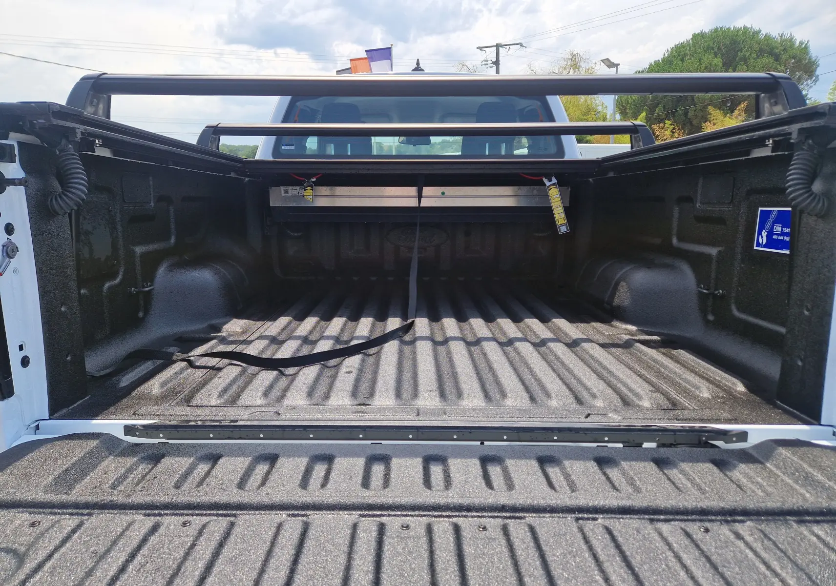 Vue arrière du plateau renforcé noir du Ford Ranger Super Cabine blanc avec rideau rigide coulissant et barres de protection.