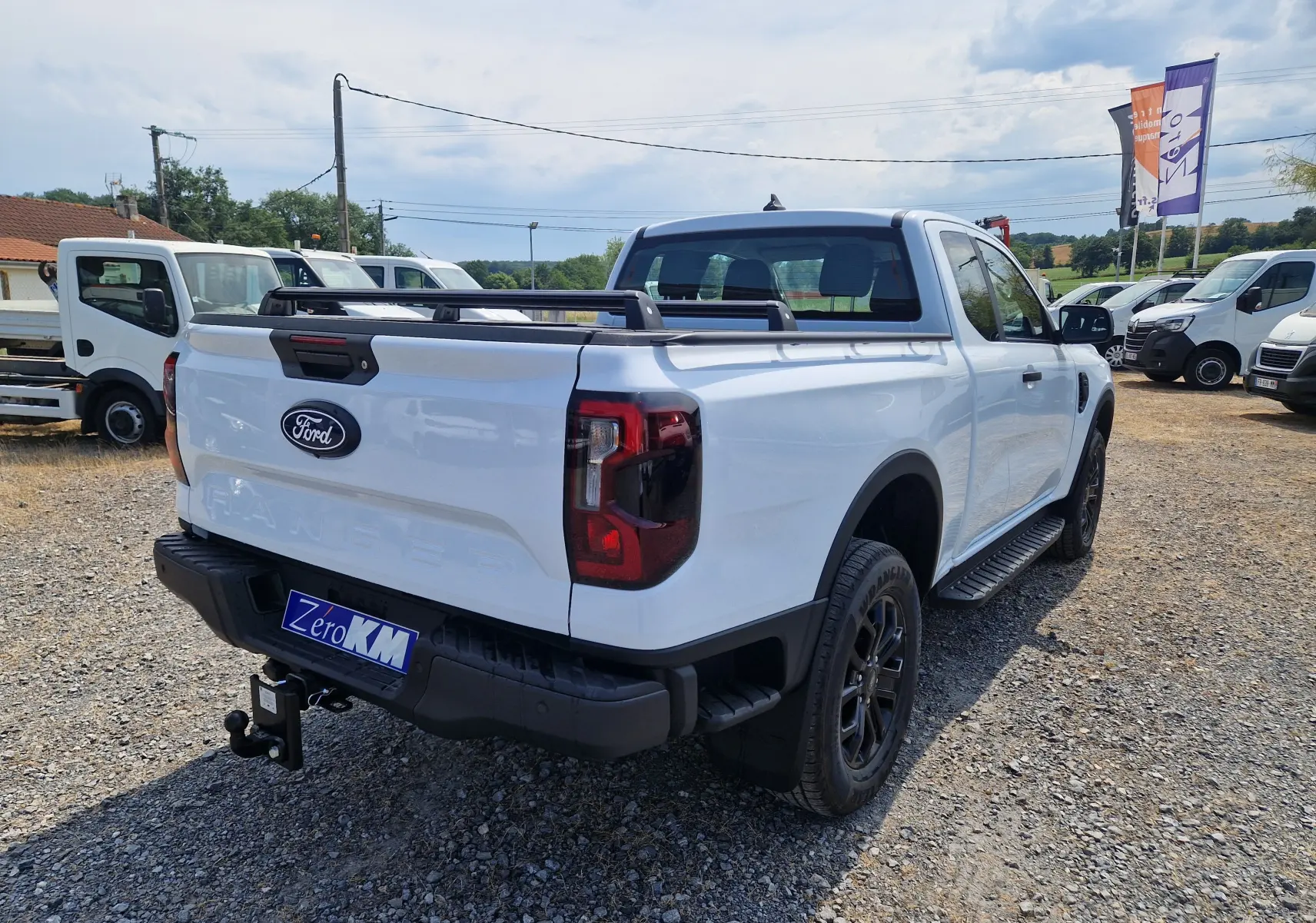 Vue 3/4 arrière droite du Ford Ranger Super Cabine blanc avec barres de plateau et marchepied noir visible.