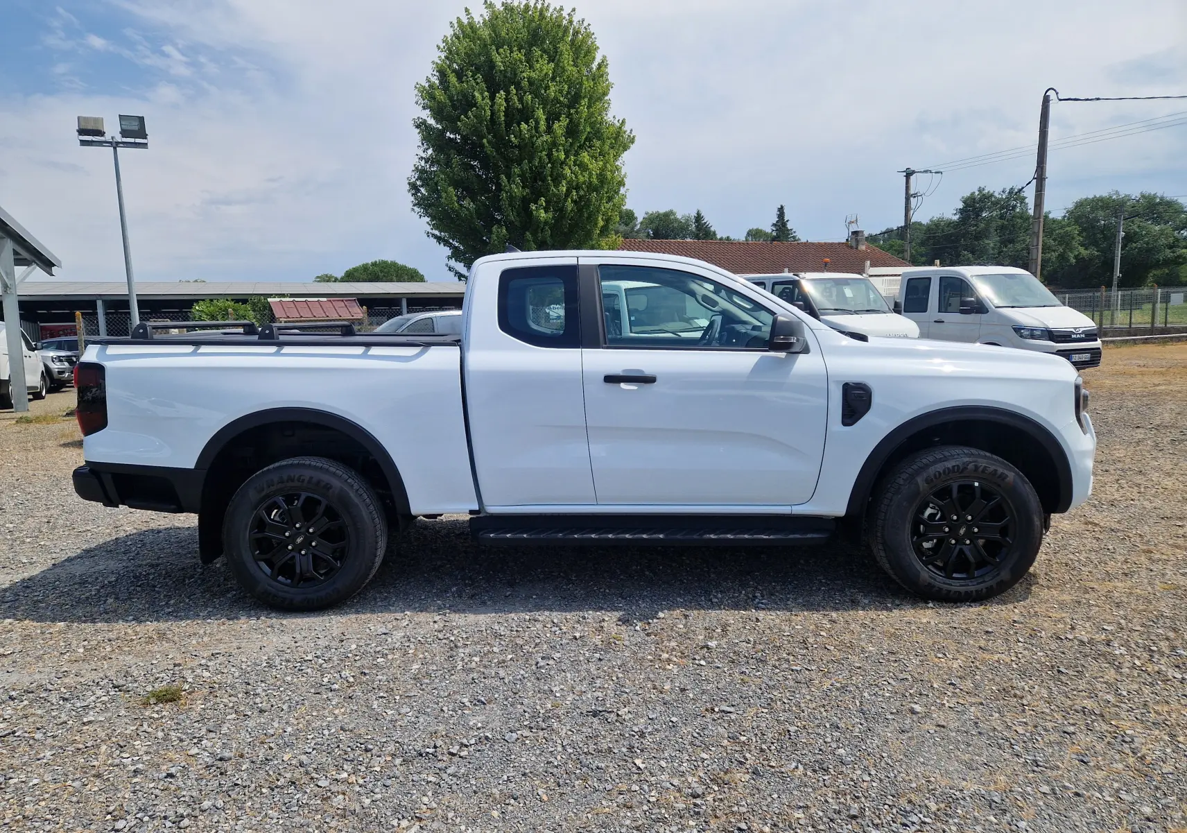 Vue de profil côté gauche d'un Ford Ranger Super Cabine blanc avec barres de toit et jantes noires.