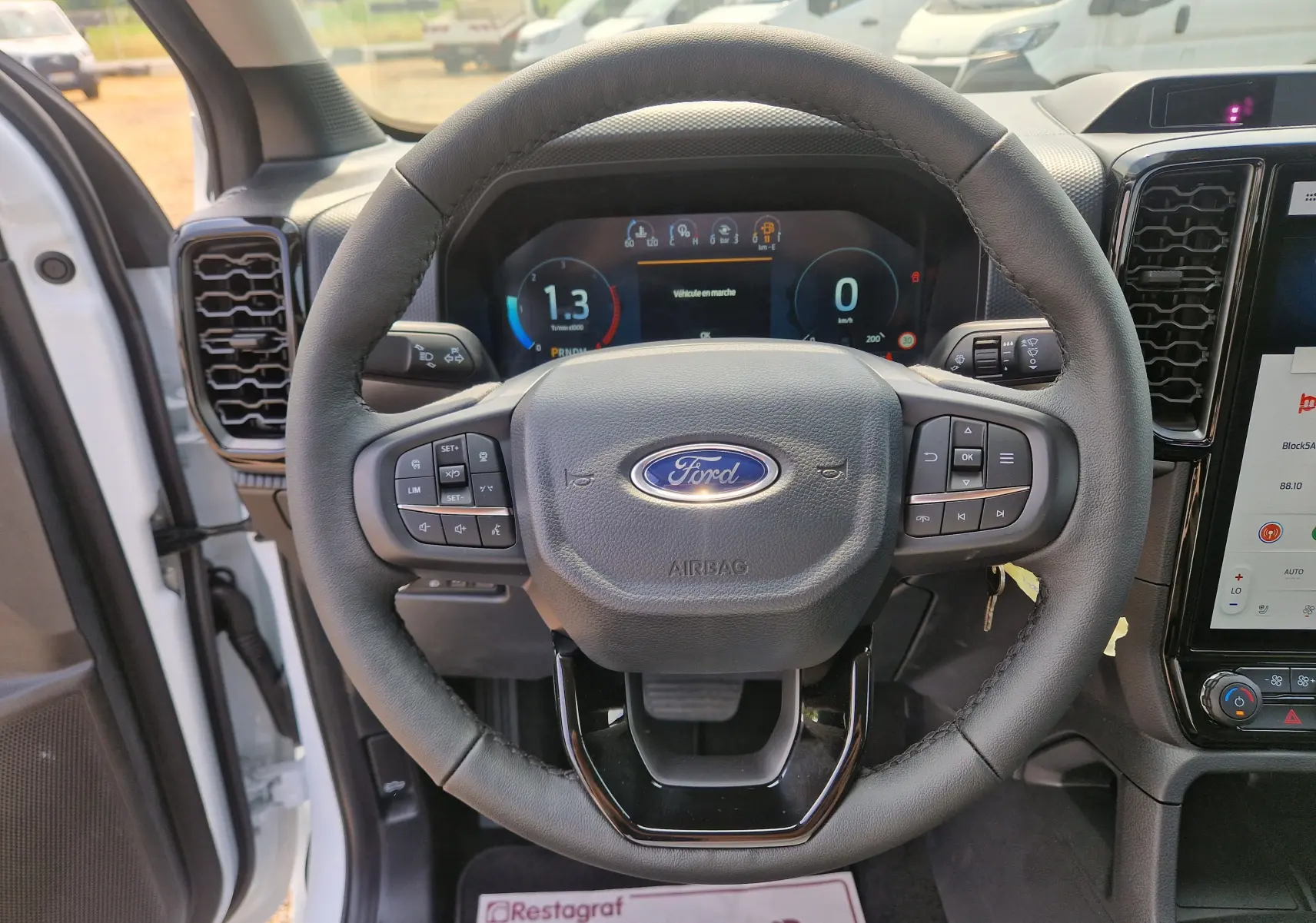 Vue intérieure centrée sur le volant noir du Ford Ranger Super Cabine blanc, avec tableau de bord digital et écran tactile visible à droite.