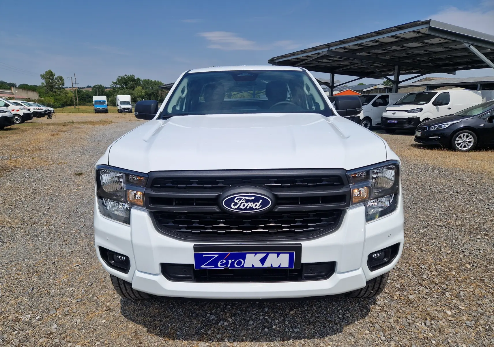 Vue frontale d'un Ford Ranger Super Cabine blanc avec calandre noire et plaque Zéro KM sur un terrain extérieur.