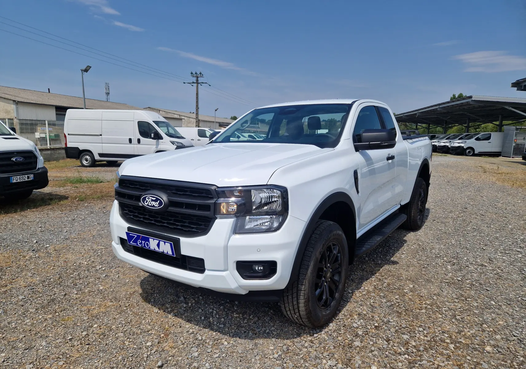 Ford Ranger Super Cabine blanc vu en 3/4 avant droit, avec calandre noire et marchepieds latéraux noirs.