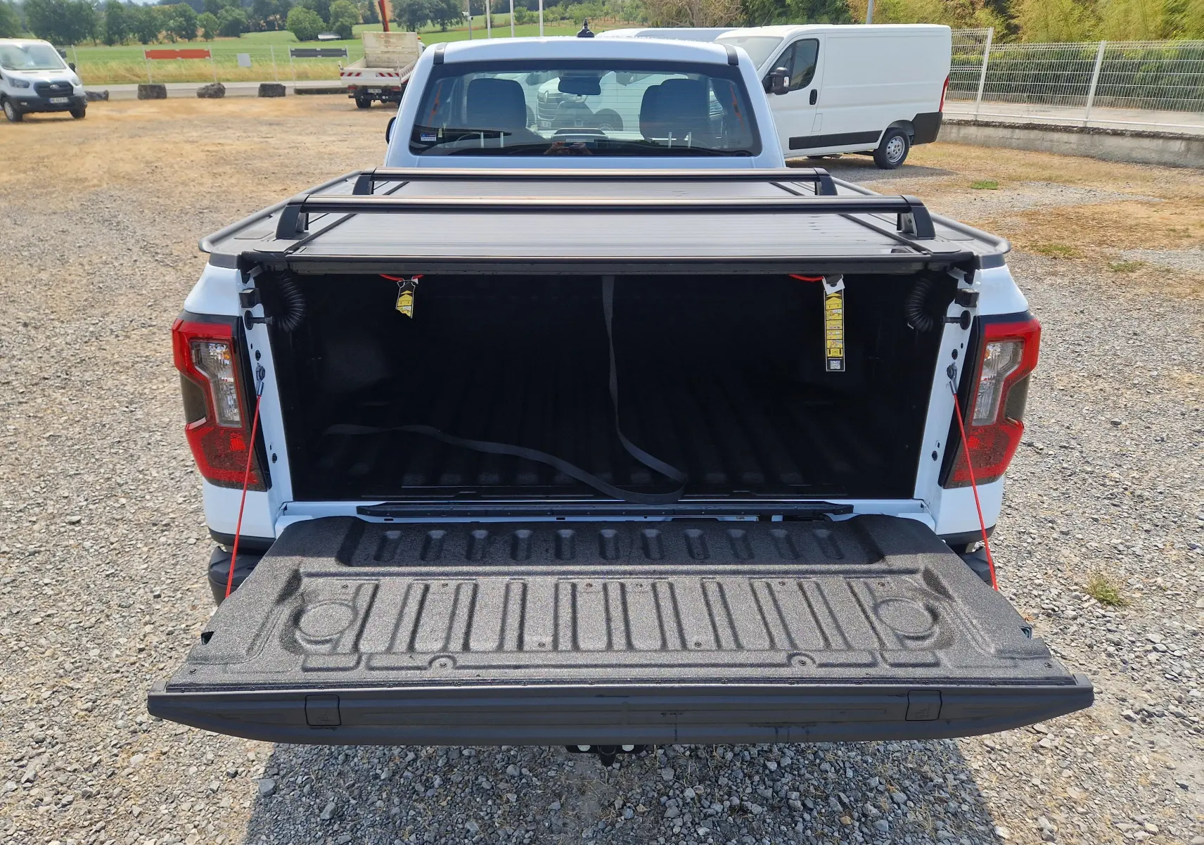 Vue arrière d'un Ford Ranger Super Cabine blanc avec plateau ouvert et rideau rigide coulissant visible.