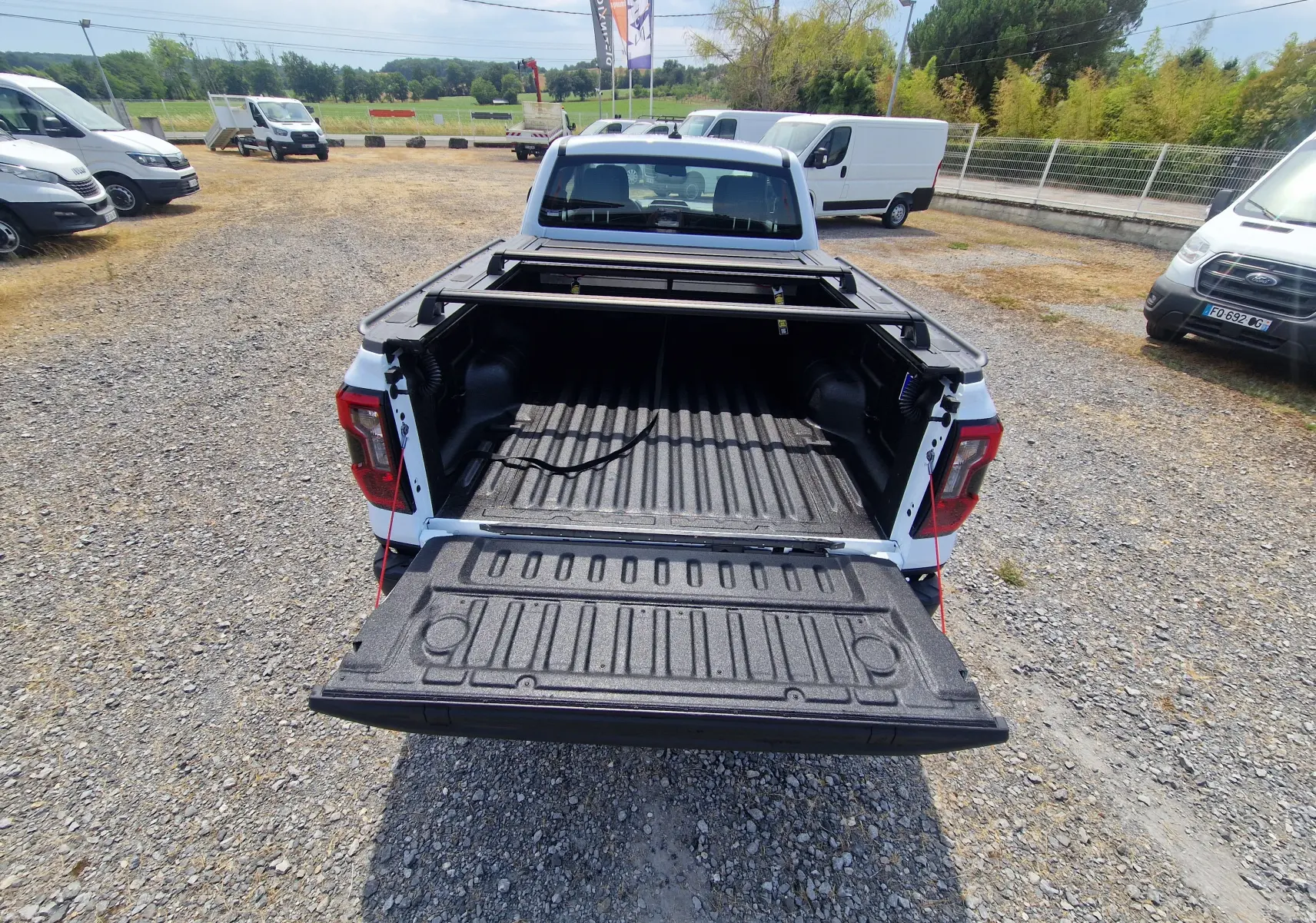 Vue arrière d’un Ford Ranger Super Cabine blanc avec plateau ouvert, rideau rigide coulissant et protection renforcée.
