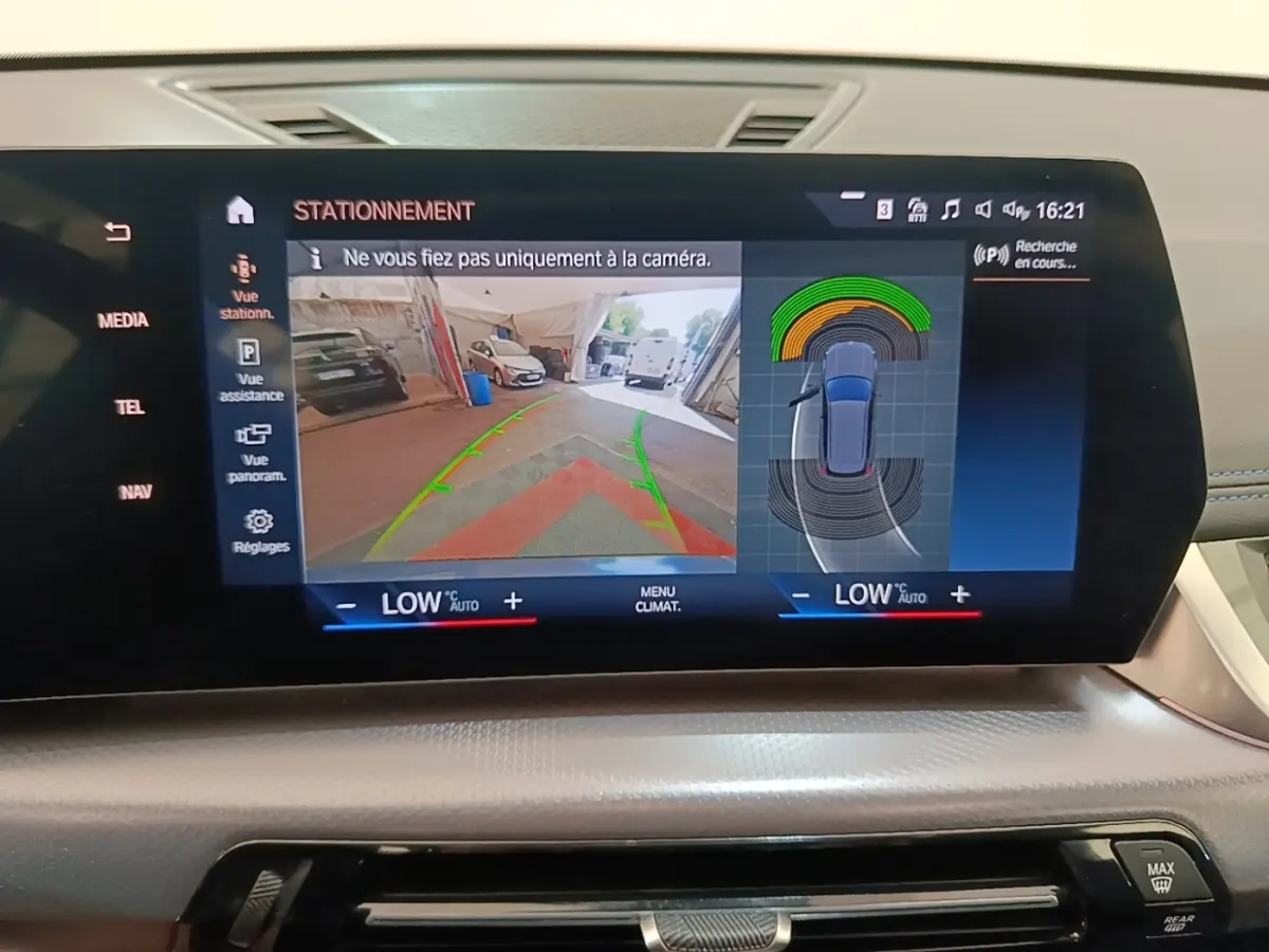 Écran tactile central du BMW X1 xDrive25e M Sport 2023 montrant l'aide au stationnement avec vue caméra arrière et capteurs.