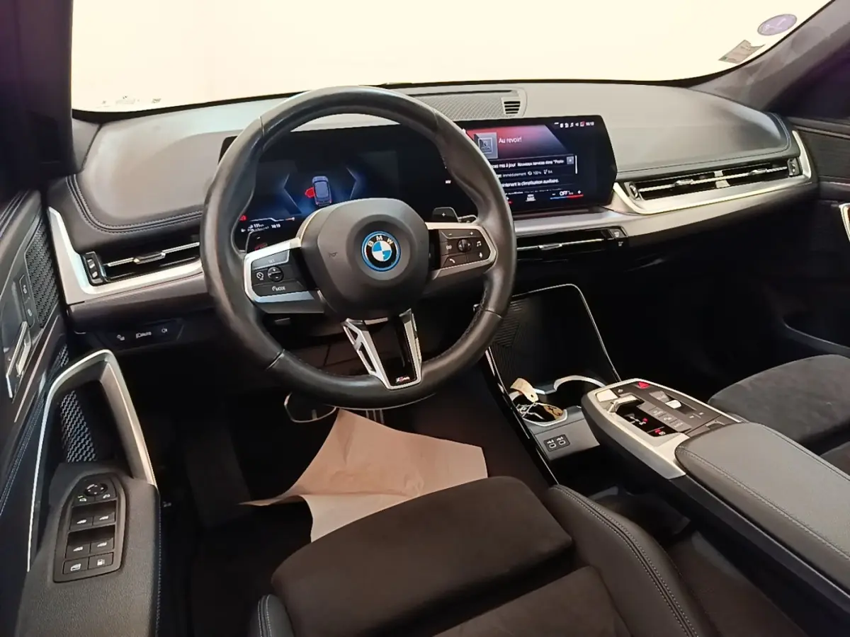 Vue intérieure du poste de conduite BMW X1 xDrive25e M Sport 2023, volant cuir alu et écran tactile large.