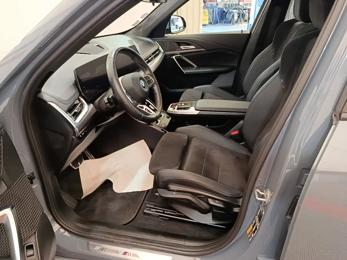 Vue intérieure côté conducteur du BMW X1 xDrive25e M Sport gris foncé, volant cuir alu multifonctions et sièges sport noirs.