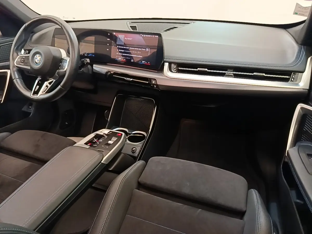 Intérieur BMW X1 xDrive25e M Sport 2023, vue avant côté conducteur, tableau de bord noir avec écran tactile large.