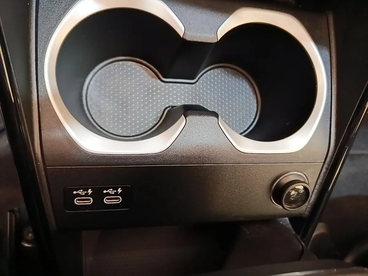 Gros plan sur les ports USB-C et prise 12V sous les porte-gobelets noirs d’un BMW X1 xDrive25e gris foncé.