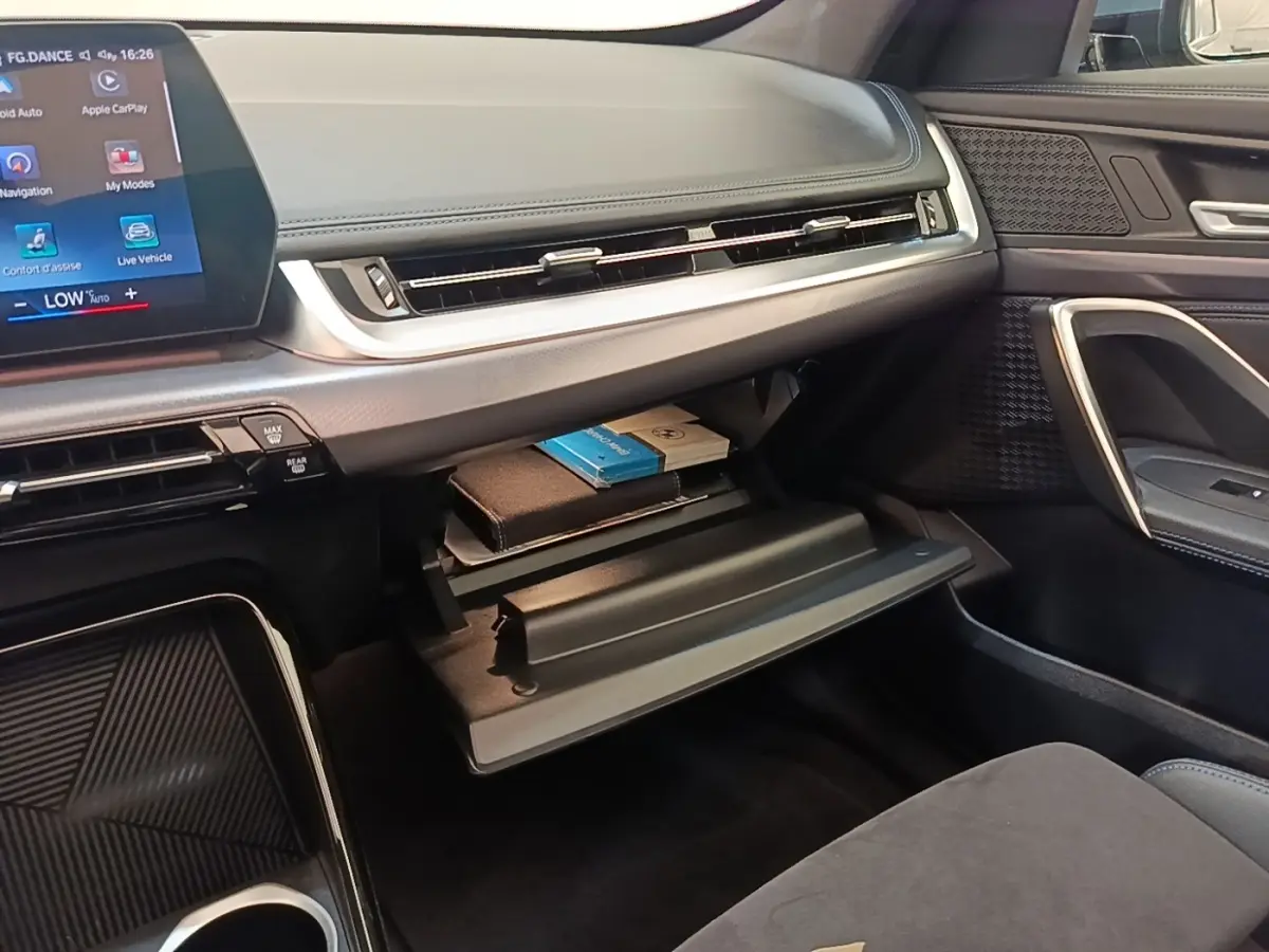 Intérieur BMW X1 xDrive25e M Sport 2023, vue côté passager sur boîte à gants ouverte avec tableau de bord gris foncé.